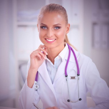 Güzel, genç, gülümseyen bayan doktor masada oturuyor ve yazıyor..