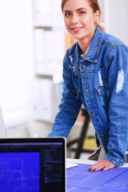 Enstrümanlar, planlar ve dizüstü bilgisayarlarla masanın yanında duran genç bir kadın.