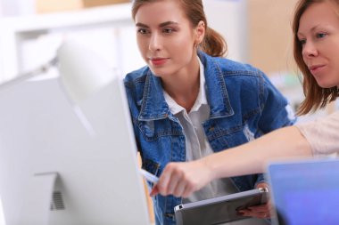 Masanın yanında duran iki genç kadın enstrüman, plan ve dizüstü bilgisayarla