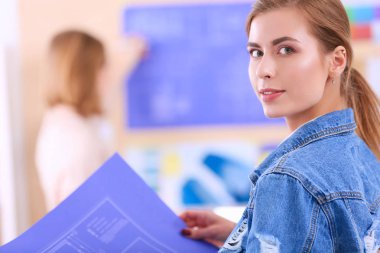 Masanın yanında duran iki genç kadın enstrüman, plan ve dizüstü bilgisayarla