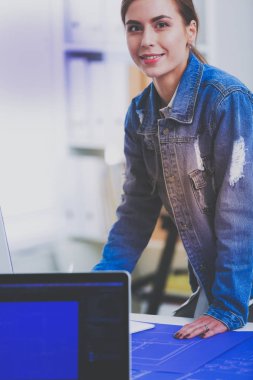 Enstrümanlar, planlar ve dizüstü bilgisayarlarla masanın yanında duran genç bir kadın.