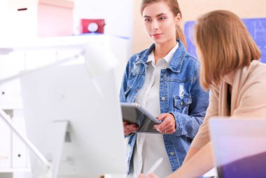 Masanın yanında duran iki genç kadın enstrüman, plan ve dizüstü bilgisayarla