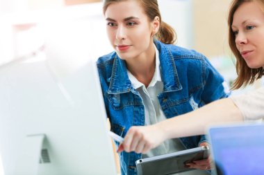 Masanın yanında duran iki genç kadın enstrüman, plan ve dizüstü bilgisayarla