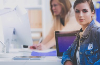 İki genç kadın masada enstrümanlar, planlar ve dizüstü bilgisayarlarla oturuyor.