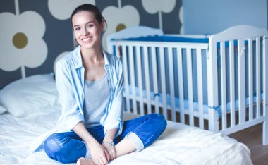 Yatakta çocuk karyolası yakın oturan genç kadın.