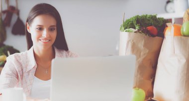 kahve fincanı ve dizüstü evde mutfakta gülümseyen genç kadın