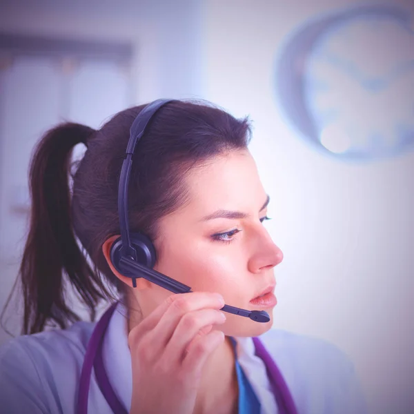 Doctor wearing headset sitting behind a desk with laptop over grey background