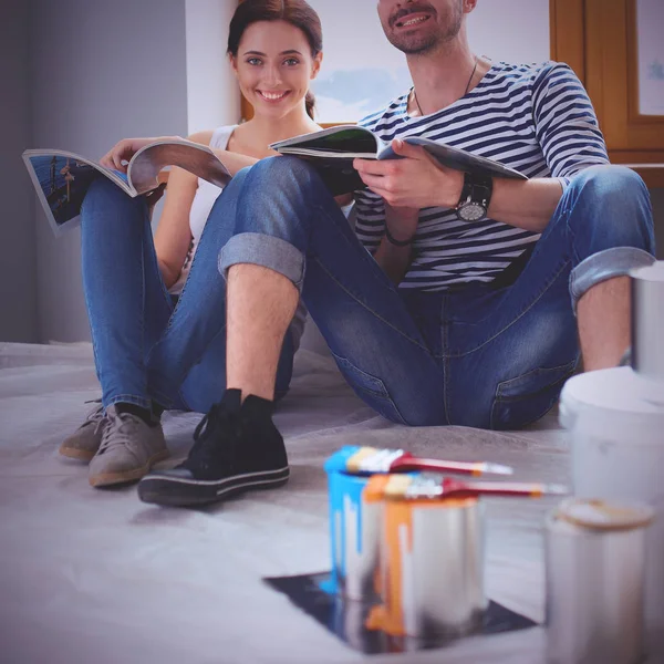 Atraktivní pár na domácí podlahy při pohledu na časopis a usmívá se na sebe. — Stock fotografie