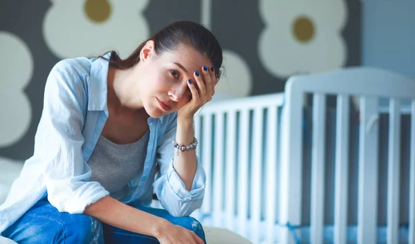 Unga trött kvinna som sitter på sängen nära barnens barnsäng. — Stockfoto