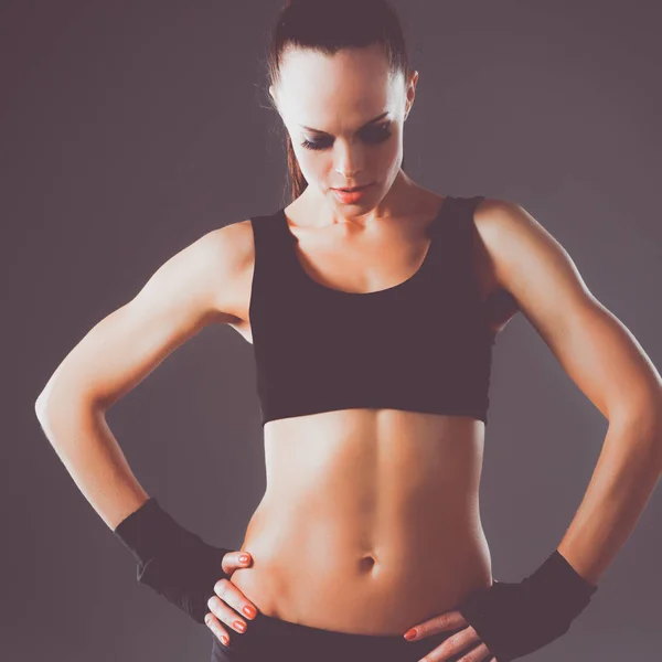 Muskulöse junge Frau steht auf grauem Hintergrund. — Stockfoto
