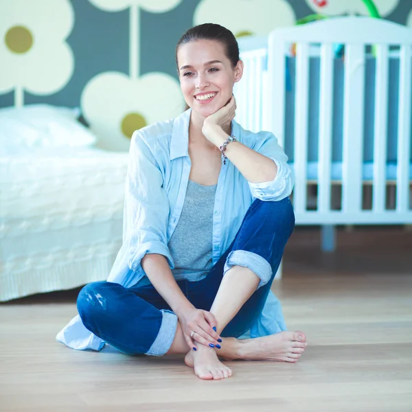 Ung kvinna sitter på golvet nära barnens barnsäng. — Stockfoto