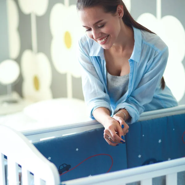 Ung kvinna som står nära barnens barnsäng. — Stockfoto