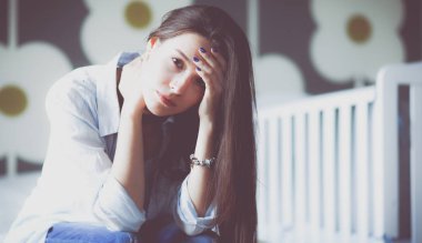 Yatakta çocuk karyolası yakın oturan genç yorgun kadın