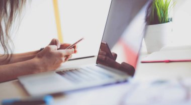 Ofis masasında dizüstü bilgisayarıyla oturan genç bir kadın.