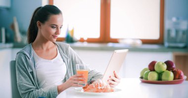 Mutfakta portakal suyu ve tableti olan genç bir kadın.