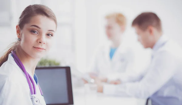 Bonito jovem sorridente médico feminino sentado na mesa — Fotografia de Stock