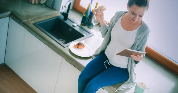 Hermosa joven usando una tableta digital en la cocina — Foto de Stock