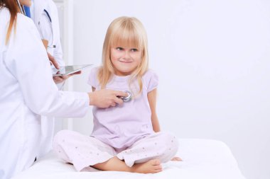 Kadın doktor ameliyatta steteskopla çocuğu muayene ediyor.