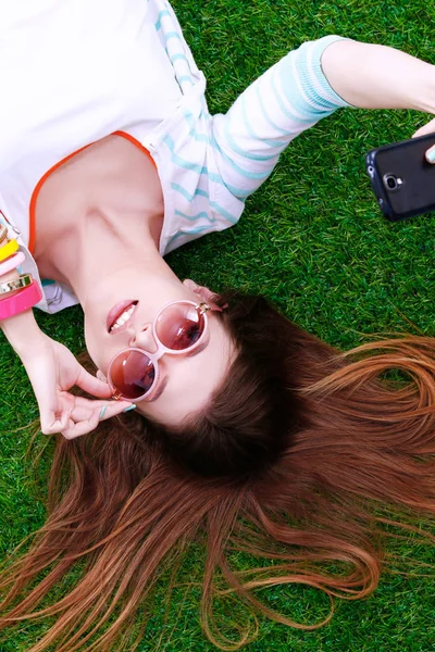 Lachende jonge vrouw liggend op het gras en het maken van een selfie — Stockfoto