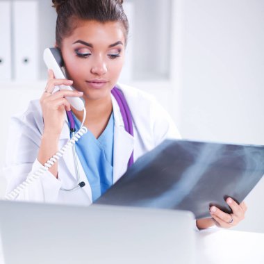 Röntgen taraması yapan kadın doktor teşhis merkezinde telefonla konuşuyor, masada oturuyor.