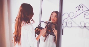 Genç ve güzel bir kadın aynanın yanında makyaj yapıyor.