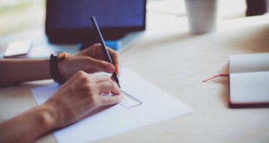 Masasında enstrümanlar, planlar ve dizüstü bilgisayarlarla oturan genç bir kadın.