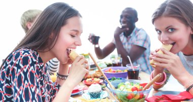 Bir grup insan ahşap masada otururken birlikte yemek yiyorlar.