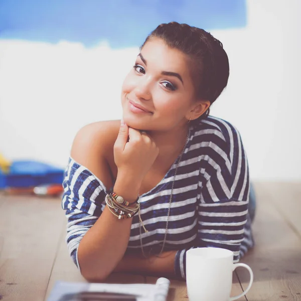 Retrato de pintora tendida en el suelo cerca de la pared después de pintar y sostener una taza — Foto de Stock