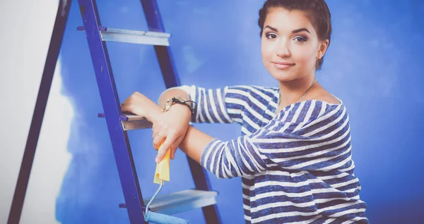 Gelukkig mooie jonge vrouw doet wandschildering, staande op de ladder — Stockfoto