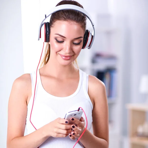 Mulher com fone de ouvido ouvindo música de pé em casa — Fotografia de Stock