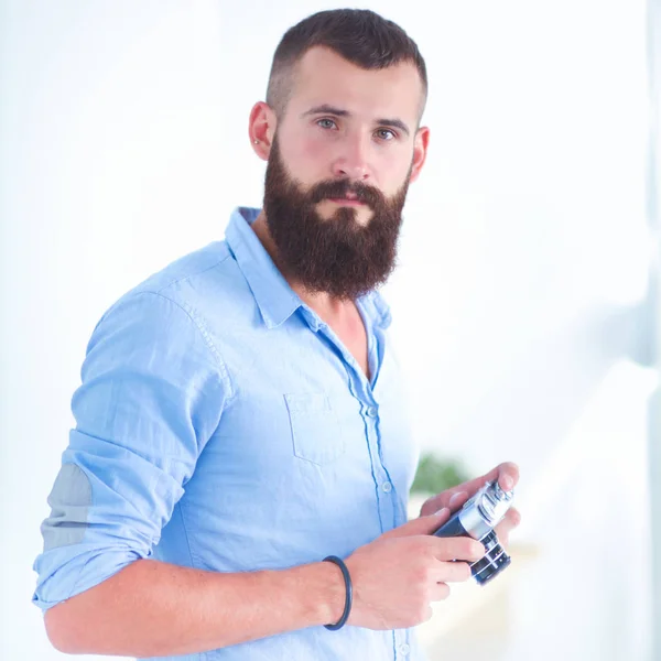 Young beard man holding a camera while standing against white b — Stock Photo, Image