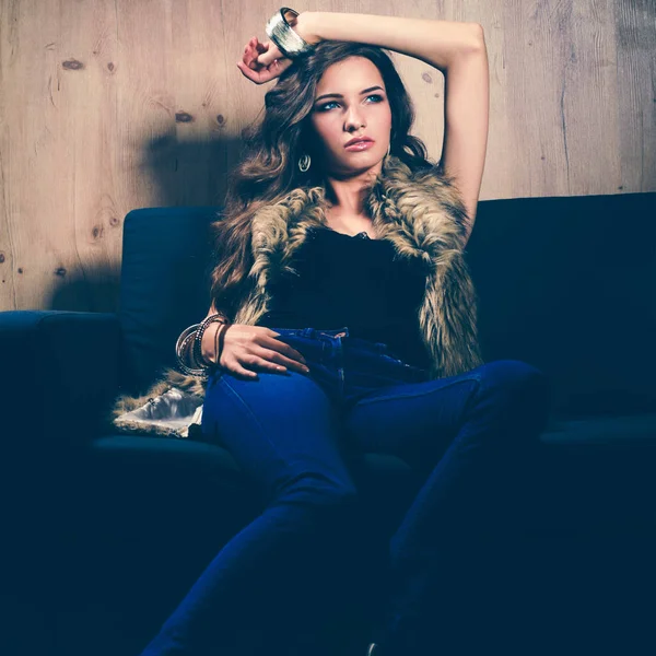 Porträt einer eleganten Frau, die auf einem schwarzen Sofa sitzt und ein blaues — Stockfoto