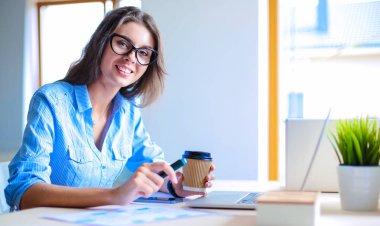 Dizüstü bilgisayar ekranına bakarak office tablosunda oturan genç kadın