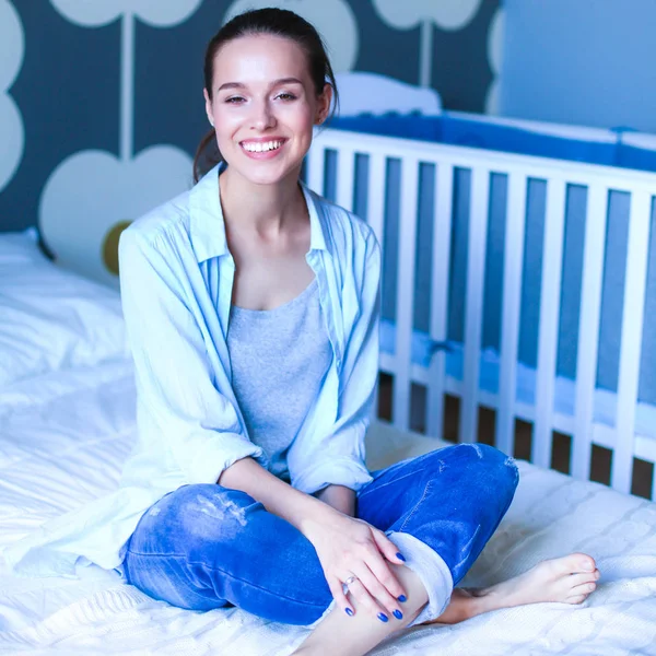 Jonge vrouw zittend op het bed in de buurt van childrens kinderbed — Stockfoto