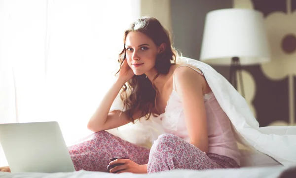 Dizüstü bilgisayar ile yatakta oturan genç güzel kadın — Stok fotoğraf