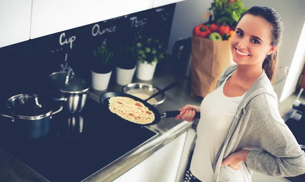 Mujer joven cocinando panqueques en la cocina de pie cerca de la estufa —  Fotos de Stock