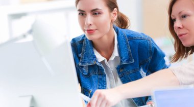 Masanın yanında duran iki genç kadın enstrüman, plan ve dizüstü bilgisayarla