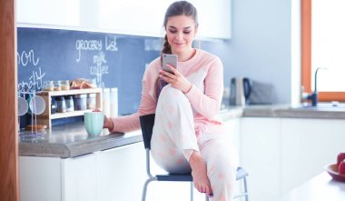 modern mutfakta otururken cep telefonu kullanan kadın