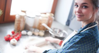 Güzel bir kadın mutfakta pasta pişiriyor. Masanın yanında duruyor.