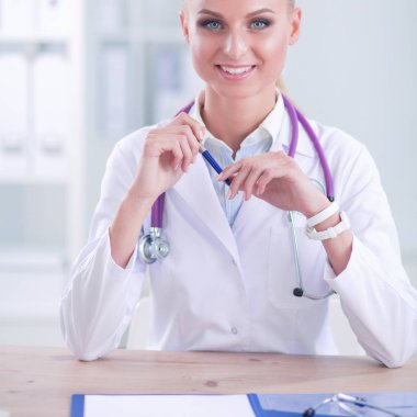 Güzel, genç, gülümseyen bayan doktor masada oturuyor ve yazıyor..