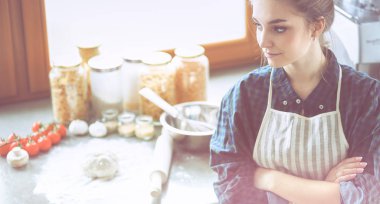 Güzel bir kadın mutfakta pasta pişiriyor. Masanın yanında duruyor.
