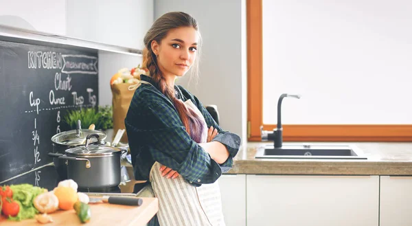 Young woman standing by the stove in the kitchen — Stock Photo, Image