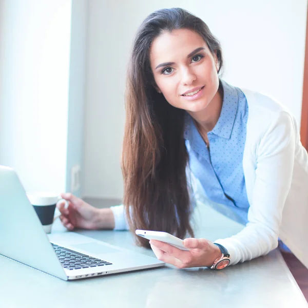 Jeune femme debout près du bureau avec ordinateur portable — Photo