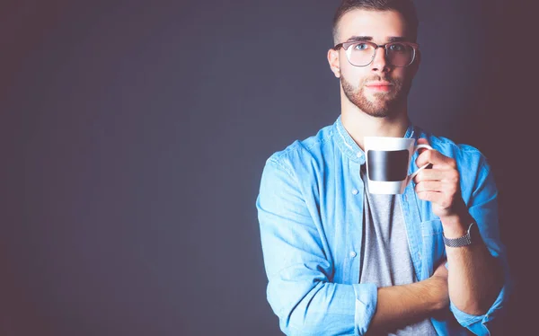 Portret knappe jonge man standing en holding kopje koffie in zijn handen — Stockfoto