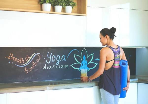 Retrato de una mujer sonriente sosteniendo en su mano una esterilla de yoga mientras está de pie en el estudio — Foto de Stock