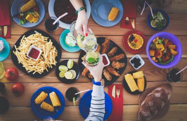 Ahşap masada otururken birlikte yemek yiyen bir grup insanın üst düzey görüntüsü. Masada yemek var. İnsanlar fast food yiyor..