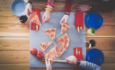 Ahşap masada otururken birlikte yemek yiyen bir grup insanın üst düzey görüntüsü. Masada yemek var. İnsanlar fast food yiyor..