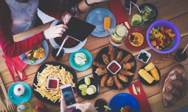Ahşap masada otururken birlikte yemek yiyen bir grup insanın üst düzey görüntüsü. Masada yemek var. İnsanlar fast food yiyor..
