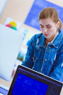 Enstrümanlar, planlar ve dizüstü bilgisayarlarla masanın yanında duran genç bir kadın..