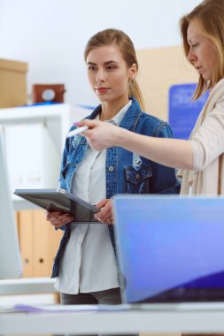 Masanın yanında duran iki genç kadın enstrüman, plan ve dizüstü bilgisayarla.